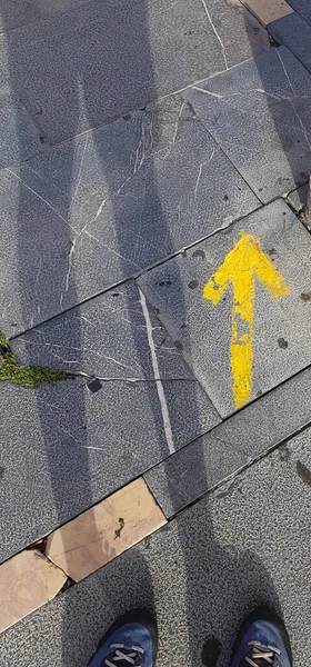 Bir hacının gölgesi ve botları sarı bir okun yanında St James Yolu 'ndaki Yol İşareti