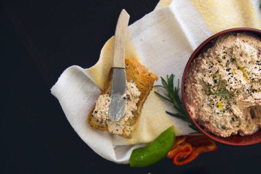 Süzme peynirli, kurutulmuş domatesli, ton balıklı, maydanozlu, siyah kimyonlu tanecikler serpiştirilmiş, tahıllı ekmek ile servis edilen siyah arka planda..