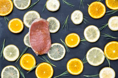 Kırmızı et dilimleri, kırmızı biberler, domatesler ve yeşil salata yaprakları koyu taş zemin üzerinde..