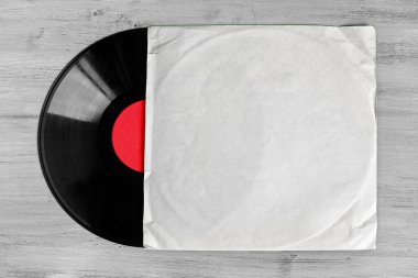 Tahta bir masanın üzerinde duran beyaz bir zarfın içindeki vinil plak.
