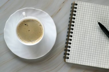 Üzerinde not defteri olan beyaz bir fincan kahve.