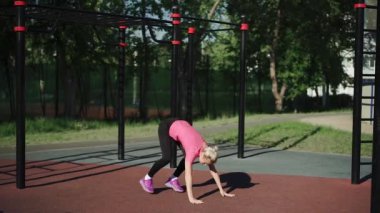 Formda bir kadın stadyumda ağır çekimde burpee egzersizi yapıyor.