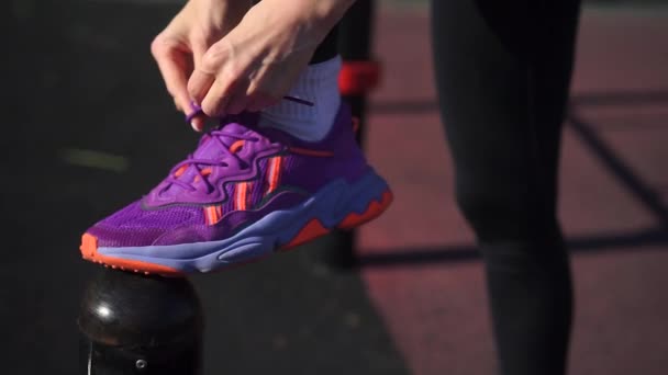 Acercamiento mujer ata cordones de zapatos en zapatillas de deporte púrpura en el estadio — Vídeo de stock