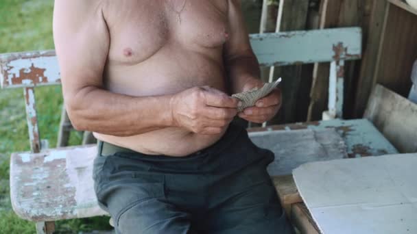 Velho com torso nu jogando cartas e sentado no velho banco azul fora — Vídeo de Stock