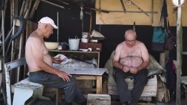 Två gubbar med bara överkroppen spelar kort i byn — Stockvideo