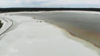 Ormanın yakınındaki göl boyunca uzanan beyaz kumların mavi gökyüzüne bakan hava manzarası. 