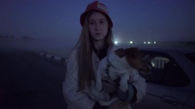 Gece vakti sislerin ve fenerlerin arkasında elinde köpek olan bir kadın.