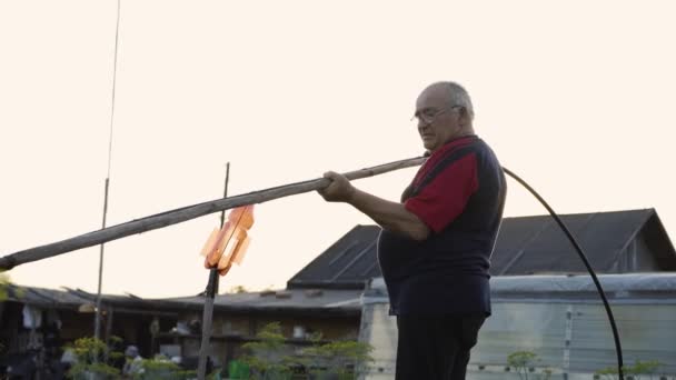 Avô regando legumes em um fundo de uma velha casa de madeira ao nascer do sol — Vídeo de Stock