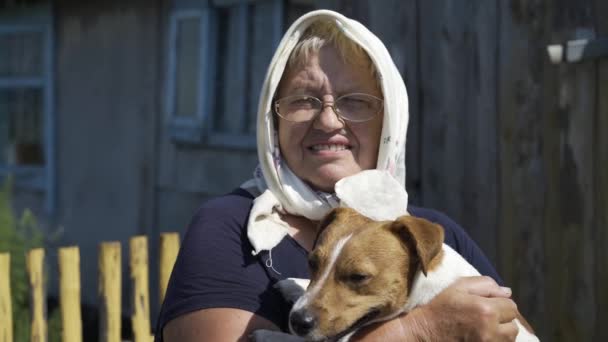 Közelkép egy mosolygó nagyiról egy fejkendőben, egy kutyával a karjában. — Stock videók