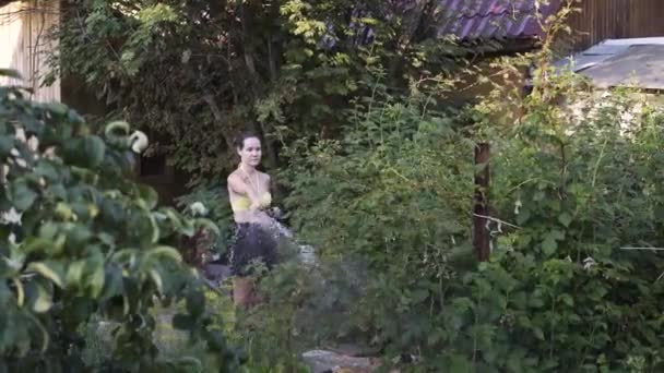 Junge Frau gießt Himbeerstrauch und lächelt im Sommer im Garten — Stockvideo