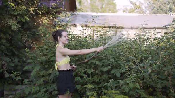 Frau im gelben Badeanzug gießt an Sommertagen Gemüse im Garten — Stockvideo