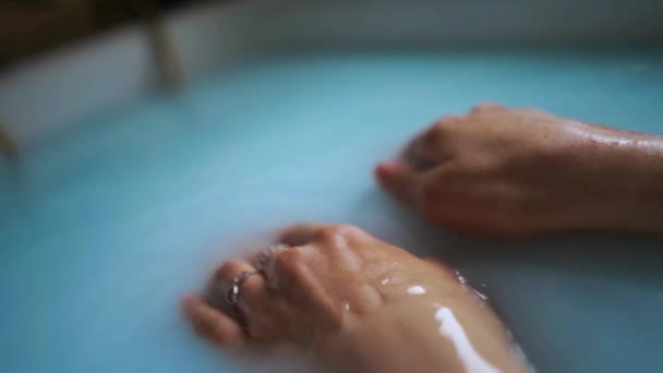 Крупним планом жіночі руки торкаються поверхні води в ванні з молоком — стокове відео