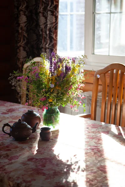 Buquê de flores silvestres na mesa à luz do sol, louça de barro na mesa — Fotografia de Stock