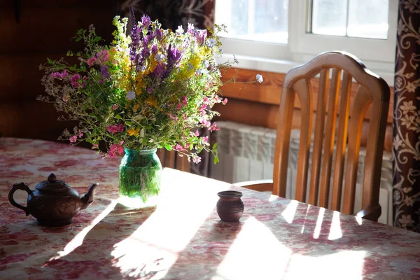 Buquê de flores silvestres na mesa à luz do sol, louça de barro na mesa, cadeira de madeira — Fotografia de Stock