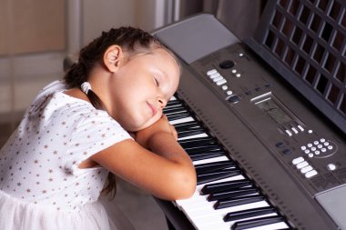 Beyaz elbiseli çocuk elektronik bir piyanonun, sentezleyicinin tuşlarında uyur.