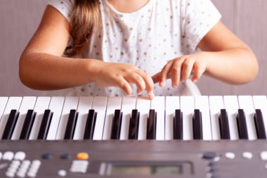 Elektronik piyano, sentezleyici çalan beyaz elbiseli bir kızın parmakları.