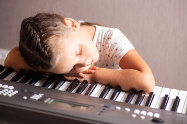 Bir çocuk, beyaz elbiseli bir kız elektronik bir piyanonun tuşlarında uyuyor, sentezleyici, kapat.