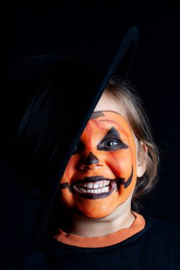 Siyah şapkalı ve yüzünde balkabağı deseni olan gülümseyen bir çocuk, Cadılar Bayramı