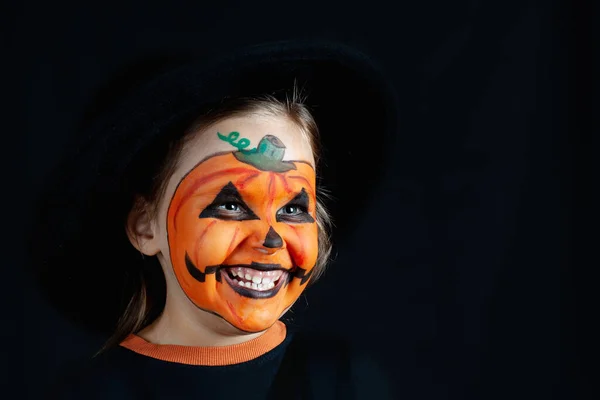 Dziewczyna w czarny kapelusz i dynia makijaż na Halloween patrzeć bokiem na czarnym tle, makiety — Zdjęcie stockowe