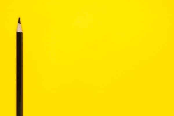 Vertical black sharp wooden pencil on a bright yellow background, isolated, copy space, mock up — Stock Photo, Image