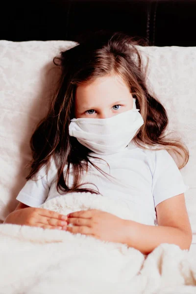 Girl close-up sitting in a white mask on the bed in the bedroom, self-isolation with a cold, the second wave of viruses — Stock Photo, Image