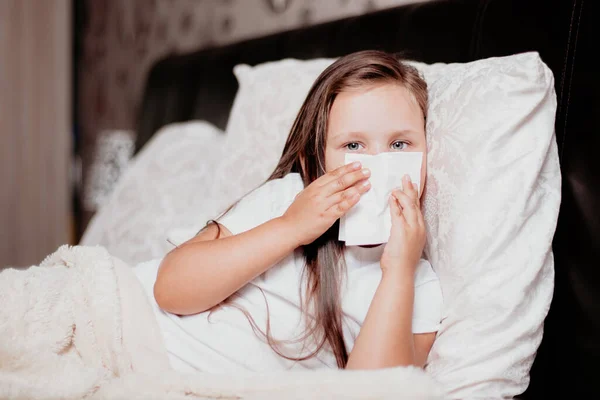 Een meisje ligt op het bed in een mooie slaapkamer, niest en bedekt haar neus met een zakdoek, de herfst koude seizoen — Stockfoto