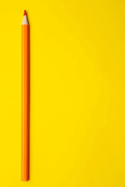 Lápis de madeira afiada laranja vertical em um fundo amarelo brilhante, isolado, espaço de cópia, mock up — Fotografia de Stock