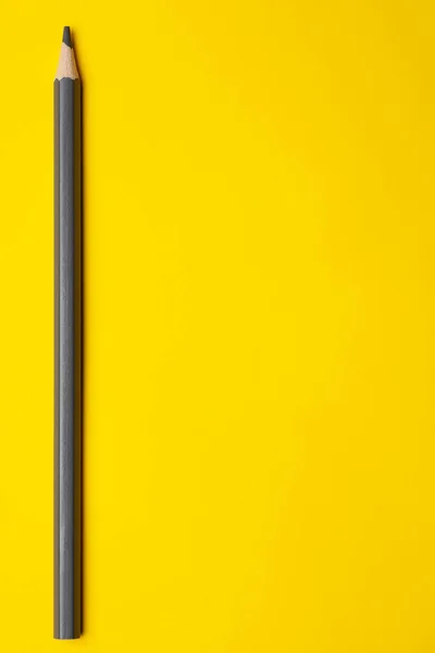 Lápiz de madera afilado gris vertical sobre un fondo amarillo brillante, aislado, espacio de copia, se burlan de — Foto de Stock