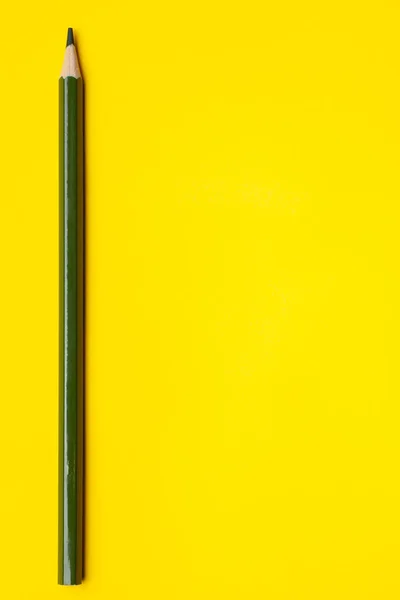 Lápis de madeira afiado verde escuro vertical em um fundo amarelo brilhante, isolado, espaço de cópia, simular — Fotografia de Stock