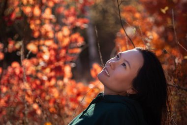 Günbatımında sonbahar ormanında gökyüzüne bakan güzel Asyalı genç bir kadının portresi.