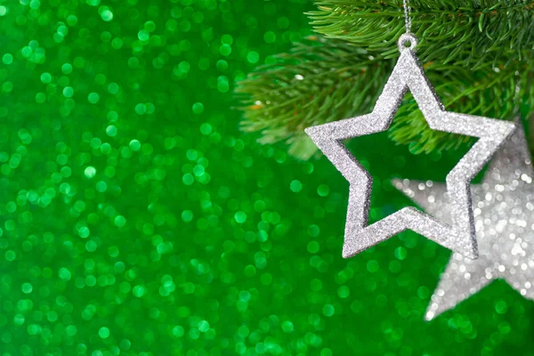 Dos estrellas de plata en una rama de árbol de Navidad sobre un fondo verde brillante de bokeh, se burlan — Foto de Stock