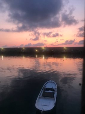 Gün batımında ışıklar ve denizde tekne yansıması.