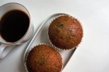 Sıcak sade kahve ve iki muzlu kek beyaz bir kabın içine yerleştirilip temiz ve lezzetli görünmesini sağlıyor.