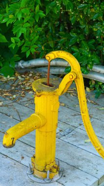 Kore çiftlik evinde eski sarı bir kuyu pompası.