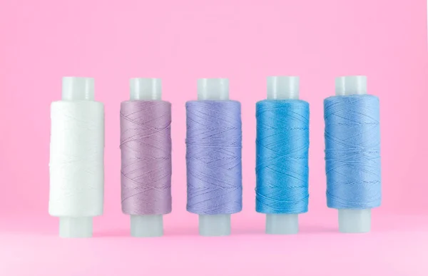 Colorful sewing threads on pink background with space for text, sewing accessories isolated, shadow of blue, violet and lilac.