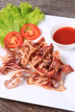 Kızarmış güneşte kavrulmuş kalamar, beyaz bir tabakta, marul ve domatesle garnitür. 