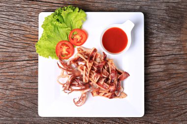 Kızarmış güneşte kavrulmuş kalamar, beyaz bir tabakta, marul ve domatesle garnitür. 