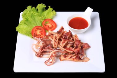 Kızarmış güneşte kavrulmuş kalamar, beyaz bir tabakta, marul ve domatesle garnitür. 