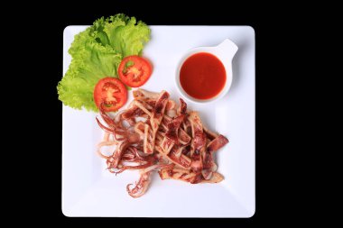 Kızarmış güneşte kavrulmuş kalamar, beyaz bir tabakta, marul ve domatesle garnitür. 