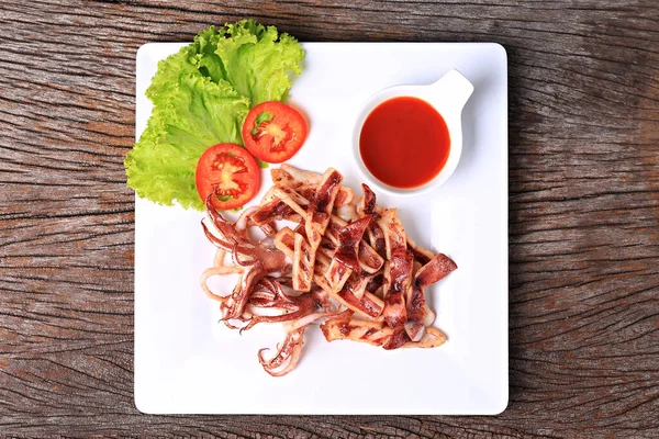 Kızarmış güneşte kavrulmuş kalamar, beyaz bir tabakta, marul ve domatesle garnitür. 