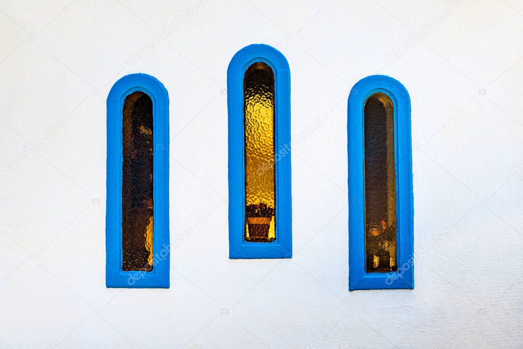 Element of the Greek church. Three narrow windows with blue edging in the white wall.