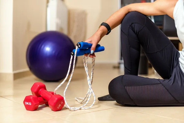Workout equipment used at home.  Fitness ball, dumbbells, skipping rope in the hand of the woman sitting on the floor.