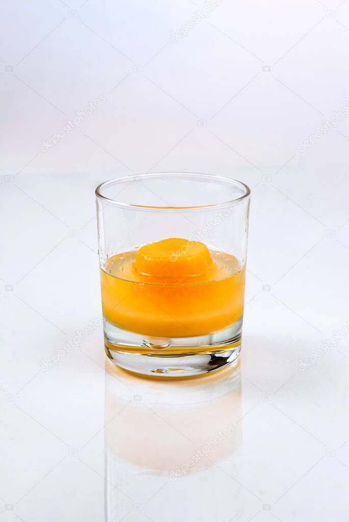 Glass with big piece of ice cube made of orange juice and white liquid or spirits like vodka, water, ouzo  on the white background