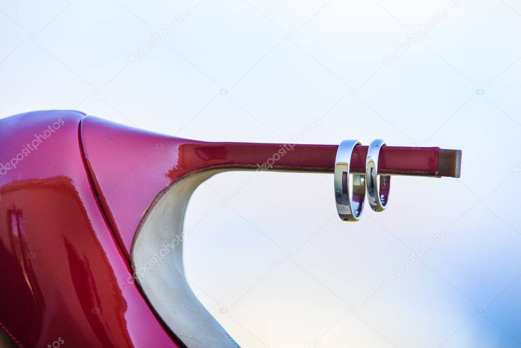 Elegant composition of wedding rings on the high heel of red wedding shoes.