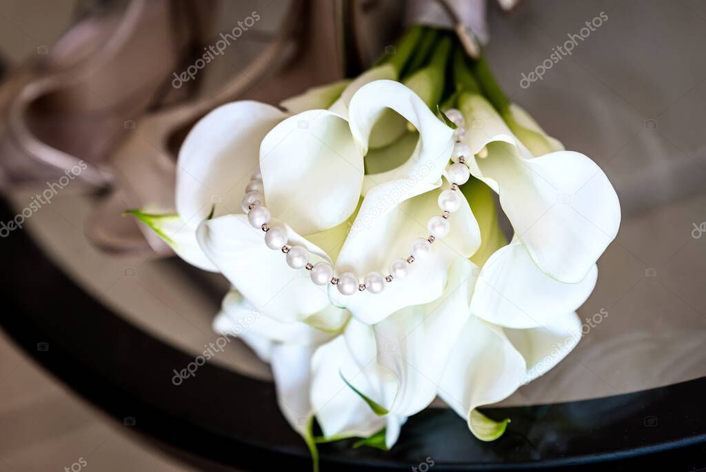 Pearl necklace on wedding bridal bouquet made of white calla lily flowers. 
