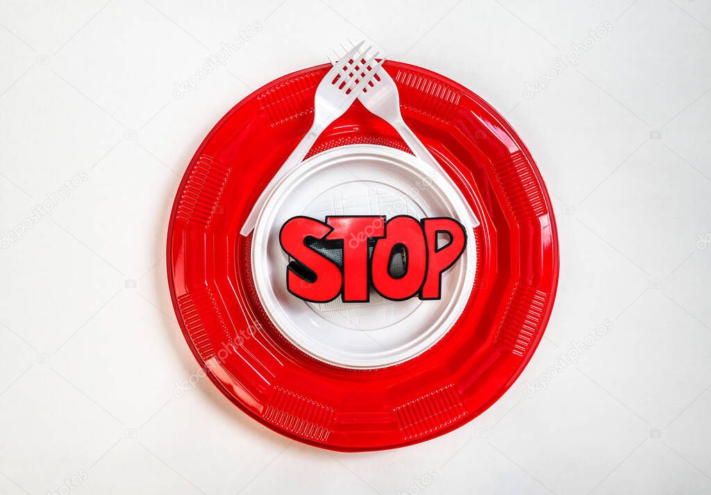 One white plastic plate in another bigger one and red, sign stop in the middle and two plastic forks crossed. Symbol of stop to use the plastic cutlery. Environment protection.