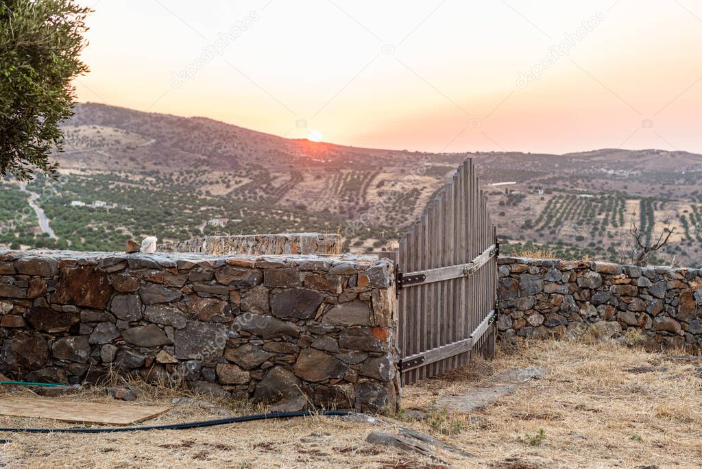 Rural mountain landscape with stone wall and closed wooden gates at sunstet time