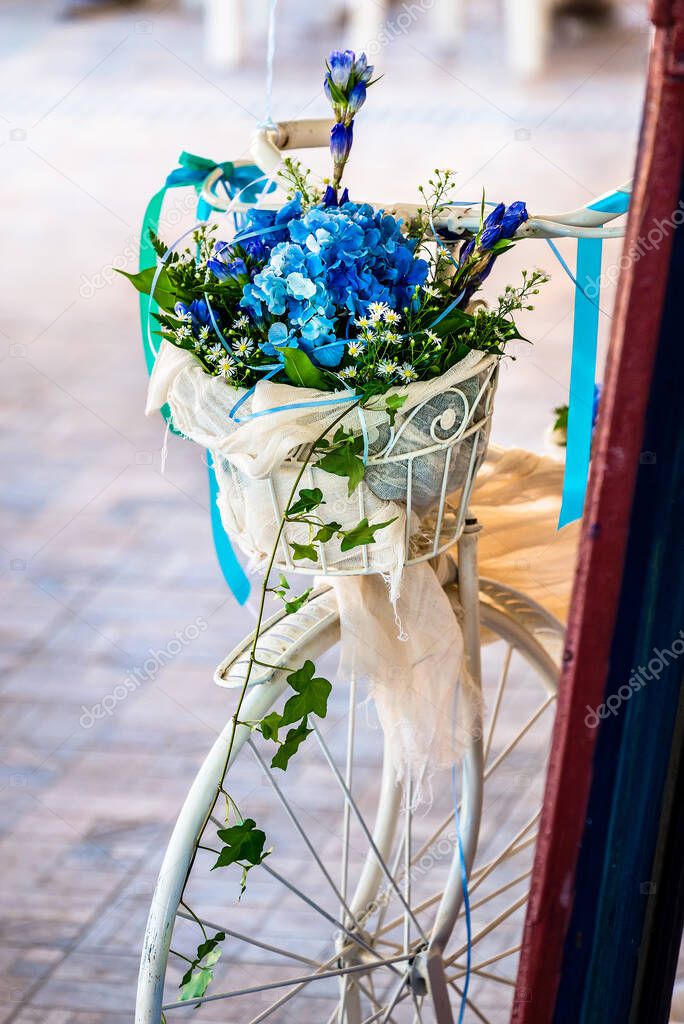 Bouquet with blue flowers hydrangea placed in the basket of the decorative white bicycle