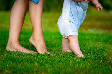 Yeşil çimenlerin üzerinde iki çocuk bacağı ve bulanık arka planda kadın bacakları.