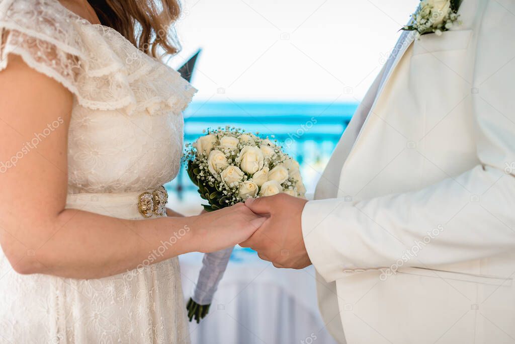 Wedding details. Holding hands of groom and bride and wedding bouquet in the middle.